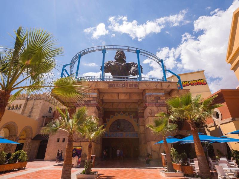 Ingresso del resort con statua, palme e cielo azzurro in un contesto di vacanza soleggiata.