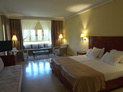 Camera d'hotel luminosa con letto matrimoniale, zona salotto e ampia finestra.