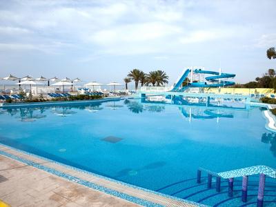 Großer Außenpool mit Wasserrutsche und Liegestühlen unter blauem Himmel.