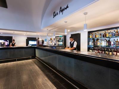 Moderne Bar mit schwarzer Theke, hellem Deckenspotlicht und Spirituosenregalen an den Wänden.