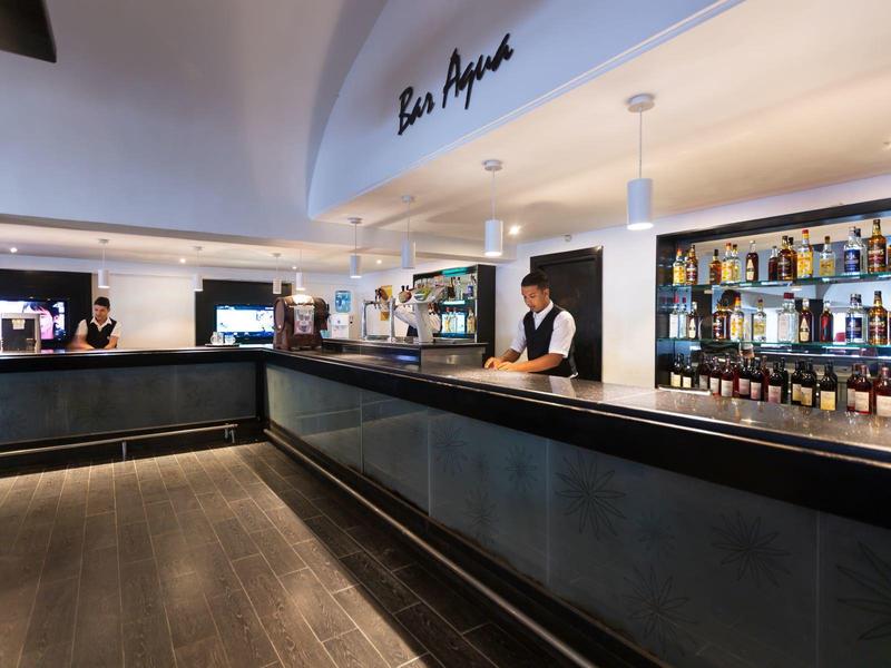 Bar moderna con barra oscura, estantes iluminados y un camarero en un hotel.