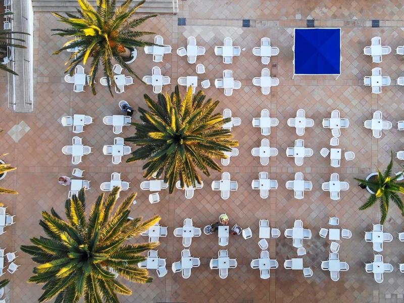 Vista aérea de un área pavimentada con mesas blancas, sillas y palmeras, ideal para hospitalidad al aire libre.