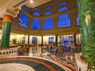 Großer Lobbybereich mit hohen Fenstern, grünen Marmorsäulen und Mosaikboden in warmem Licht.