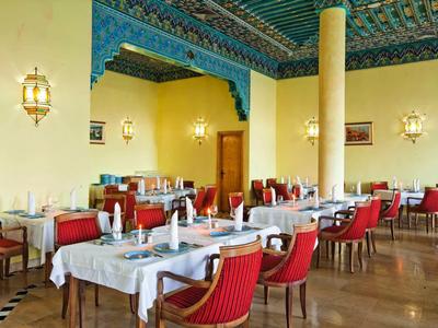 Großer Speisesaal mit weißen Tischdecken, roten Stühlen und kunstvollem blauen Deckenmuster.