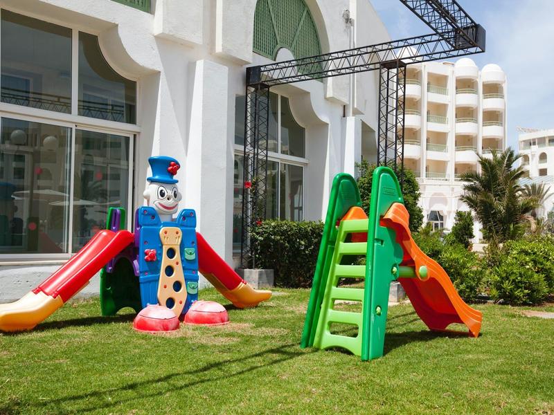 Bunter Kinderspielplatz mit Rutschen vor einem modernen Hotelgebäude.