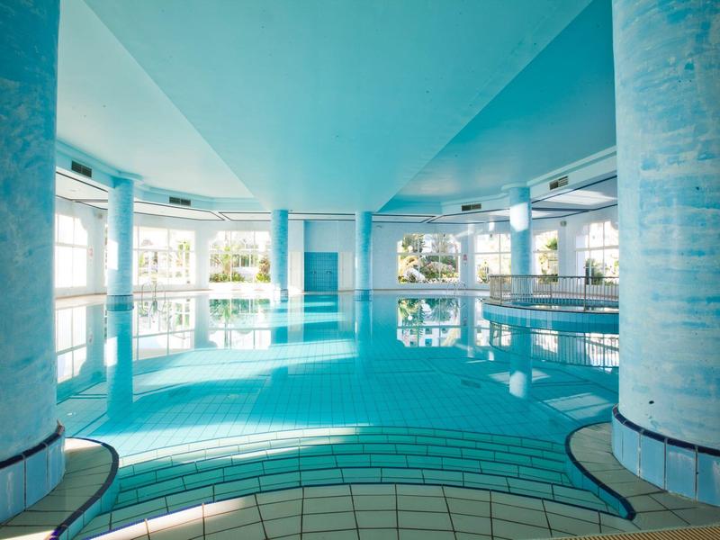 Innenbereich eines Schwimmbads mit blauen Fliesen und großen Säulen.