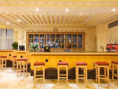 Bar moderno de hotel con mostrador de madera y varios taburetes de madera, iluminación cálida.