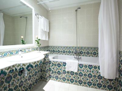 Světla koupelna s dekorativními dlaždicemi, vanou a velkým zrcadlem.