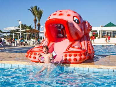 Dítě si hraje v bazénu vedle velké nafukovací červené chobotnice na skluzavce za slunečného dne.