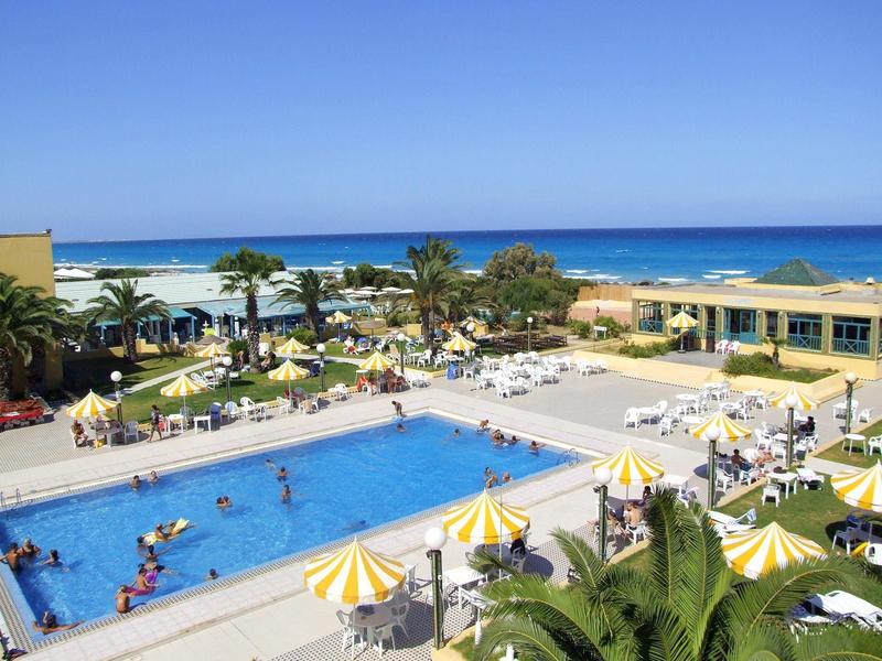 Velký venkovní bazén se žluto-bílými slunečníky a palmami u moře v resortu.