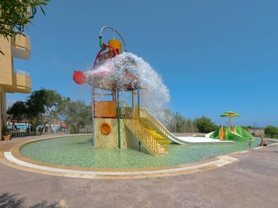 Kinderspielplatz mit Wasseranlage, gelbe Rutsche und spritzendem Wasser unter blauem Himmel.