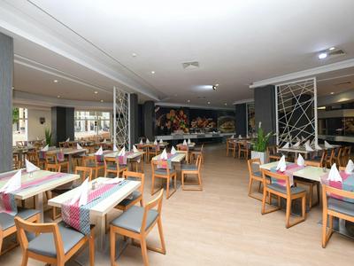 Světle osvětlená restaurace s dřevěnou podlahou, stoly s barevnými ubrousky a moderním dekorem.