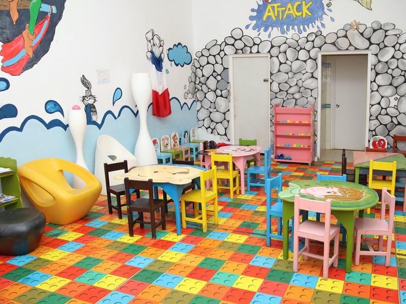 Barevná herna s dětskými stolky, židlemi a šedou kamennou nástěnnou malbou.