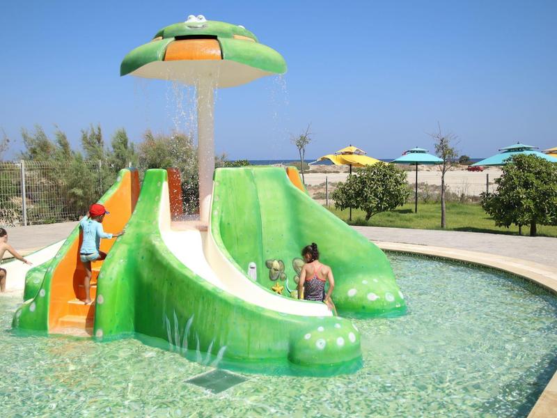 Dětský bazén s zelenou skluzavkou ve tvaru kraba a vodním prvkem venku za slunečného dne