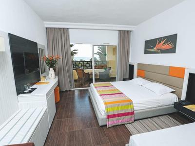 Modernes Hotelzimmer mit Doppelbett, Flachbildfernseher und Balkon mit Sitzgelegenheit.