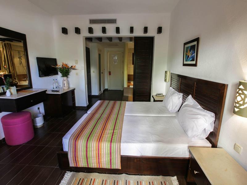 Modernes Hotelzimmer mit Doppelbett, Schreibtisch, Fernseher und dekorativen Elementen in warmen Farben.