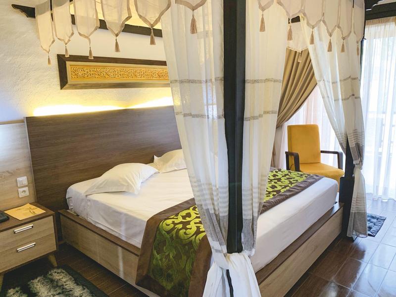 Gemütliches Doppelzimmer mit Baldachinbett, Nachttisch und Sessel neben Fenster.