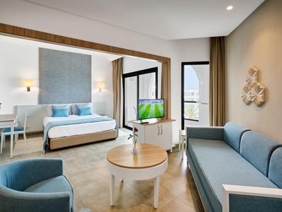 Modern eingerichtetes Hotelzimmer mit Bett, Sofa, Sesseln und Blick auf eine Terrasse.