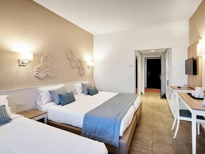 Modernes Hotelzimmer mit zwei Betten, Schreibtisch, Fernseher und warmem Licht.