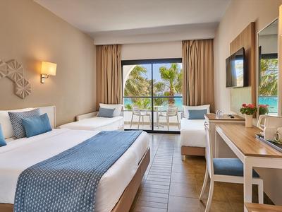 Heller Hotelzimmer mit Doppelbett, Balkon und Blick auf den Pool und Palmen.