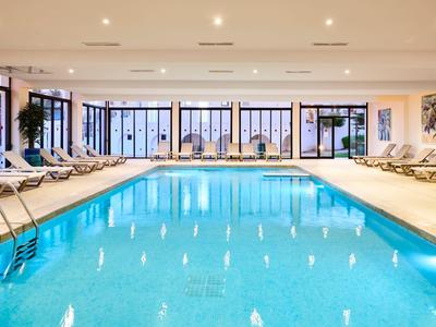 Heller Innenpool mit Liegestühlen und großen Panoramafenstern.