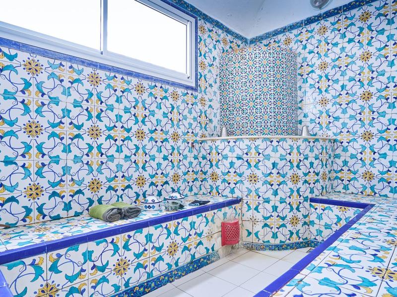 Hell gefliestes Badezimmer mit blauen, weißen und gelben Mustern und mehreren Sitz- oder Ablageflächen.