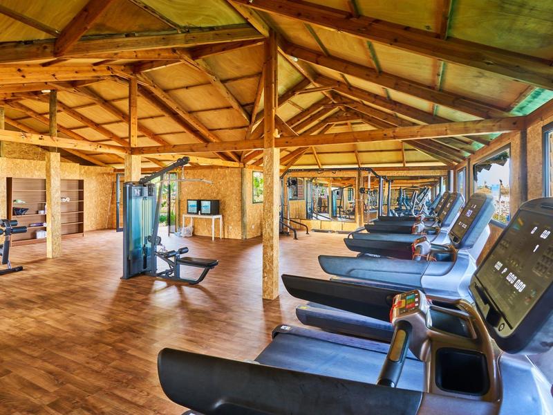 Hell und geräumig, mit Holzdach, mehreren Laufbändern, Trainingsgeräten und großen Fenstern.