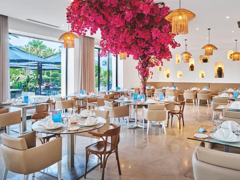 Modernes Hotelrestaurant mit bequemen Stühlen, gedeckten Tischen und einer großen pinken Blumeninstallation in der Mitte.