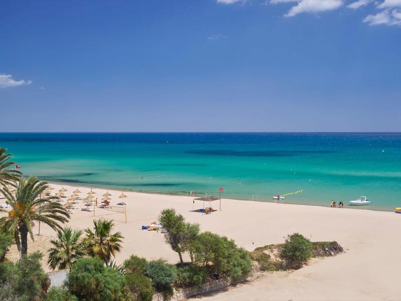 Weißer Sandstrand mit Palmen, grünblauem Meer und klarem blauem Himmel.