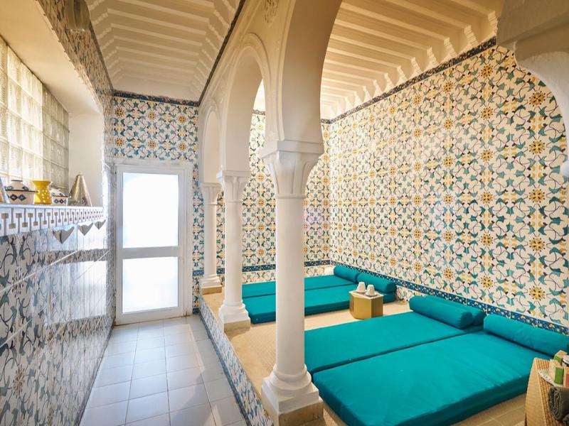 Heller Raum mit blau-grünen Sitzpolstern, kunstvollen Wandfliesen und dekorativen Säulen.