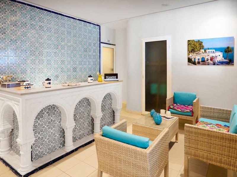 Heller Raum mit orientalischer Mosaik-Theke, Korbsesseln und blauen Kissen, Wandbild mit Meerblick.