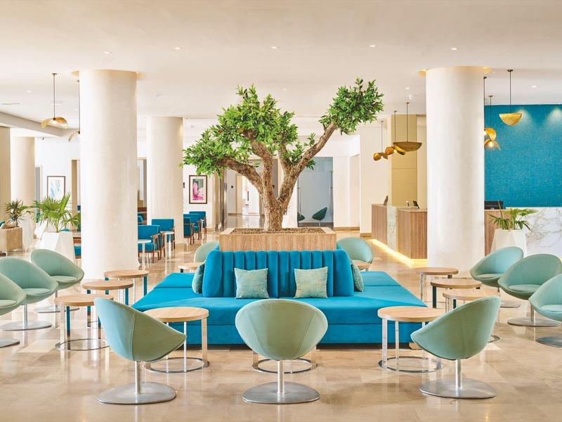 Moderner Hotel-Loungebereich mit blauem Sofa und grünen Stühlen unter einem Baum.