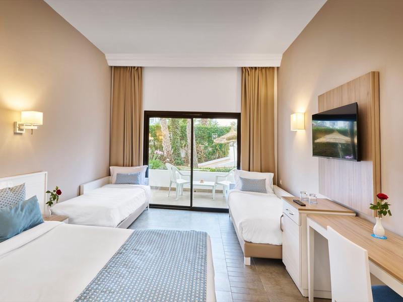 Hell eingerichtetes Hotelzimmer mit zwei Einzelbetten, großem Fenster und Terrasse mit Gartenblick.