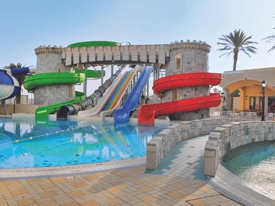 Toboggans aquatiques colorés dans un parc aquatique avec piscine et zone à thème mur de château.