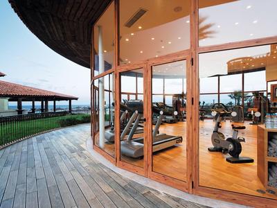 Moderner Fitnessraum mit großen Glasfenstern, Holzboden und Blick auf Terrasse und Außenbereich.