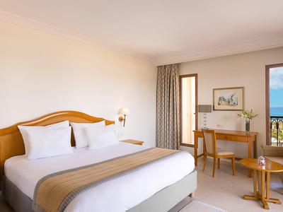 Jasny pokój hotelowy z dużym podwójnym łóżkiem, biurkiem i balkonem z widokiem na morze.