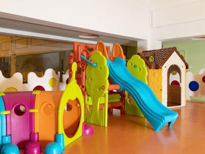 Bunter Indoor-Spielplatz mit Rutsche, Kleinkindspielzeug und einer kleinen Hütte aus Kunststoff.