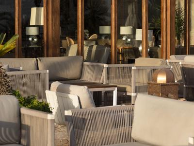 Gemütlicher Außenbereich mit Sesseln und Tischen vor großen Fenstern eines Hotels.