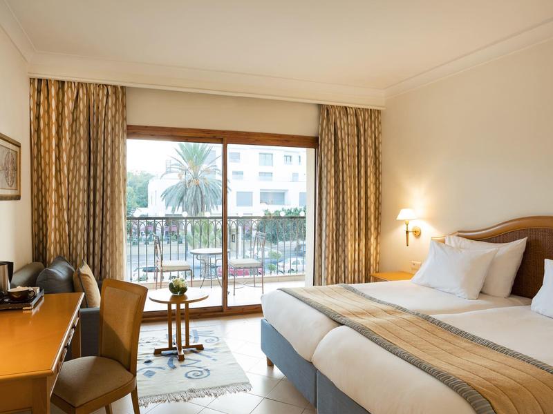 Jasny pokój hotelowy z podwójnym łóżkiem, balkonem i widokiem na basen.