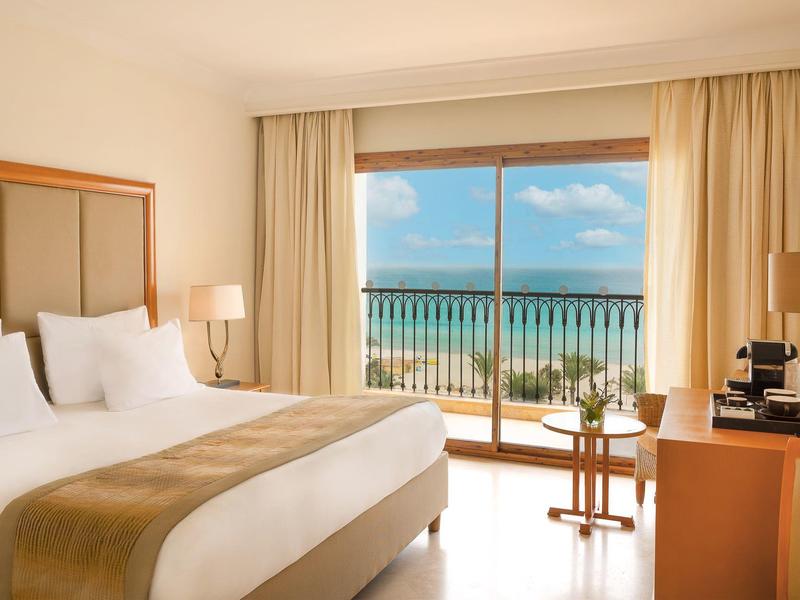 Nowoczesny pokój hotelowy z widokiem na morze i balkonem, jasne wnętrze, wygodne łóżko podwójne.