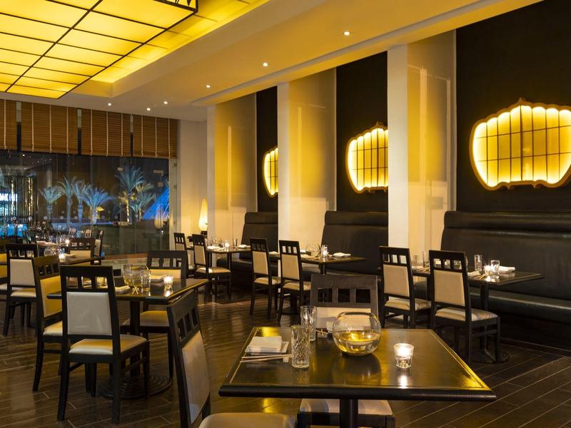 Oświetlona przestrzeń restauracyjna hotelu z nowoczesnymi stołami i krzesłami w ciepłej atmosferze.