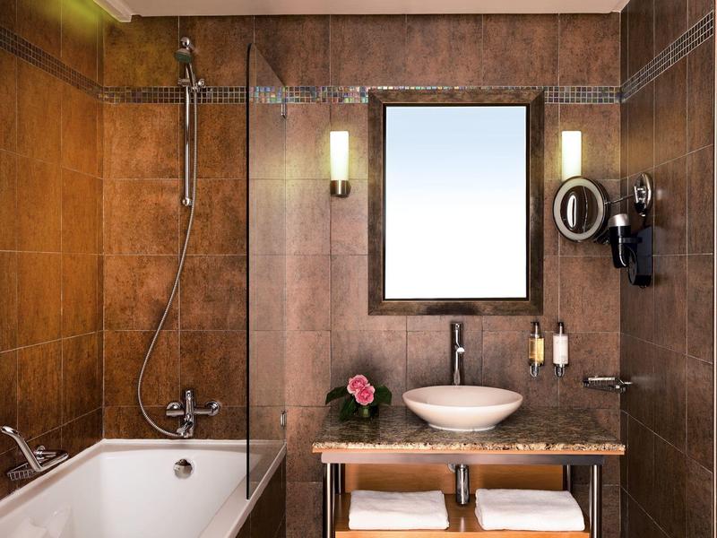Nowoczesna łazienka z wanną, umywalką i podświetlanym lustrem w ciepłych brązowych odcieniach.