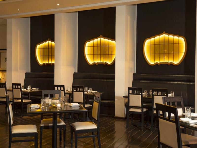 Wnętrze hotelu z ciemnymi drewnianymi meblami i ciepłym złotym oświetleniem ściennym.