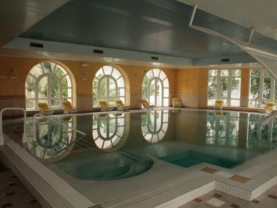 Innenpool mit sanfter Beleuchtung, umgeben von großen Rundbogenfenstern und heller Wandverkleidung.