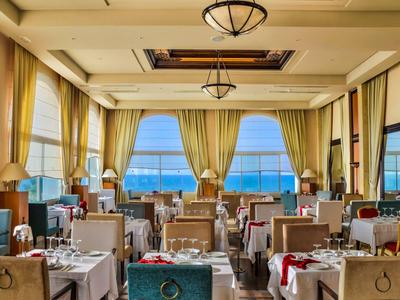 Elegantes Restaurant mit Meerblick und gedeckten Tischen in sanften Farben.