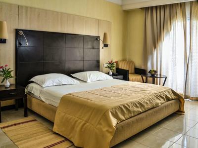 Moderní hotelový pokoj s dvojlůžkem, dvěma nočními stolky, křesly a velkým oknem s závěsy.