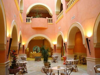 Innenhof eines Hotels mit Terrakottafarbenen Wänden, Bogenfenstern und weißen Tischen mit Stühlen.