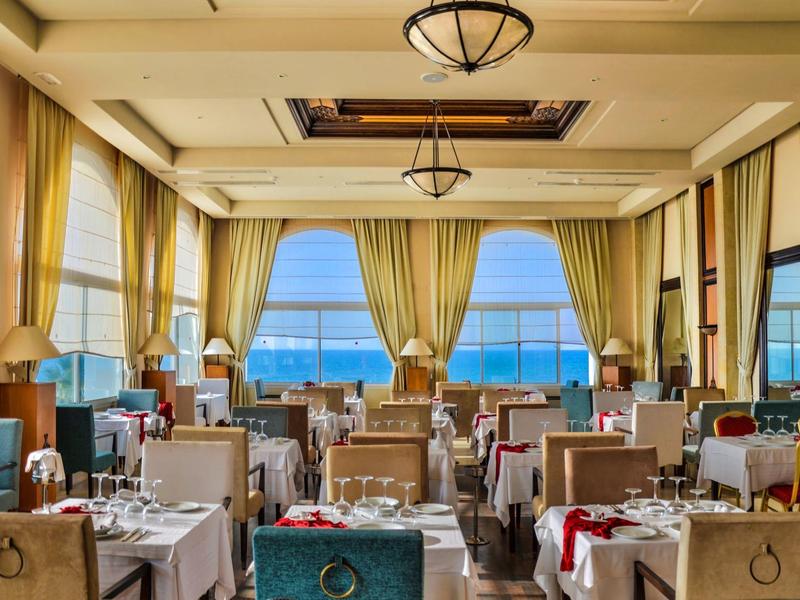 Elegantní restaurace s výhledem na moře a prostřenými stoly v jemných barvách.