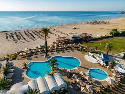 Area piscina dell'hotel con ombrelloni, palme e spiaggia sabbiosa con vista mare.