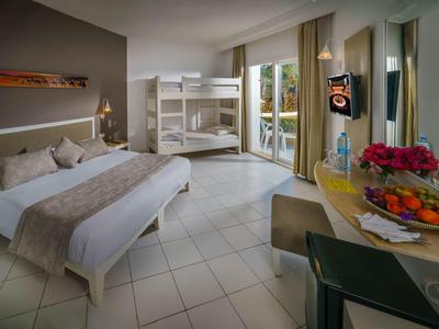 Moderní hotelový pokoj s dvoulůžkem, patrovou postelí, stolem a balkonem s výhledem na zeleň.